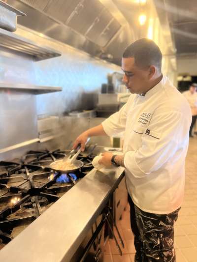 Man, dark hair, white chef coat, in kitchen making pasta